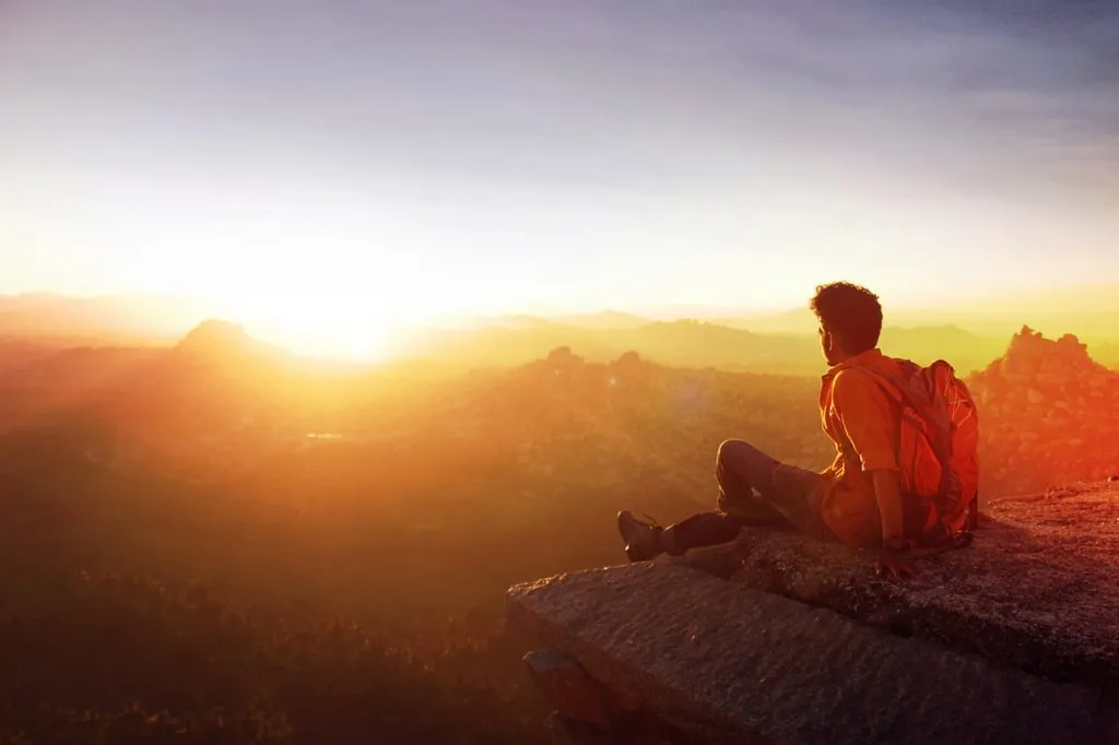 Man sitting on cliff looking at sunset